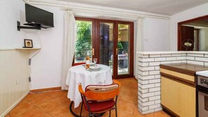 A small kitchen with a dining area, a TV mounted on the wall, and a sliding glass door leading to an outdoor area.