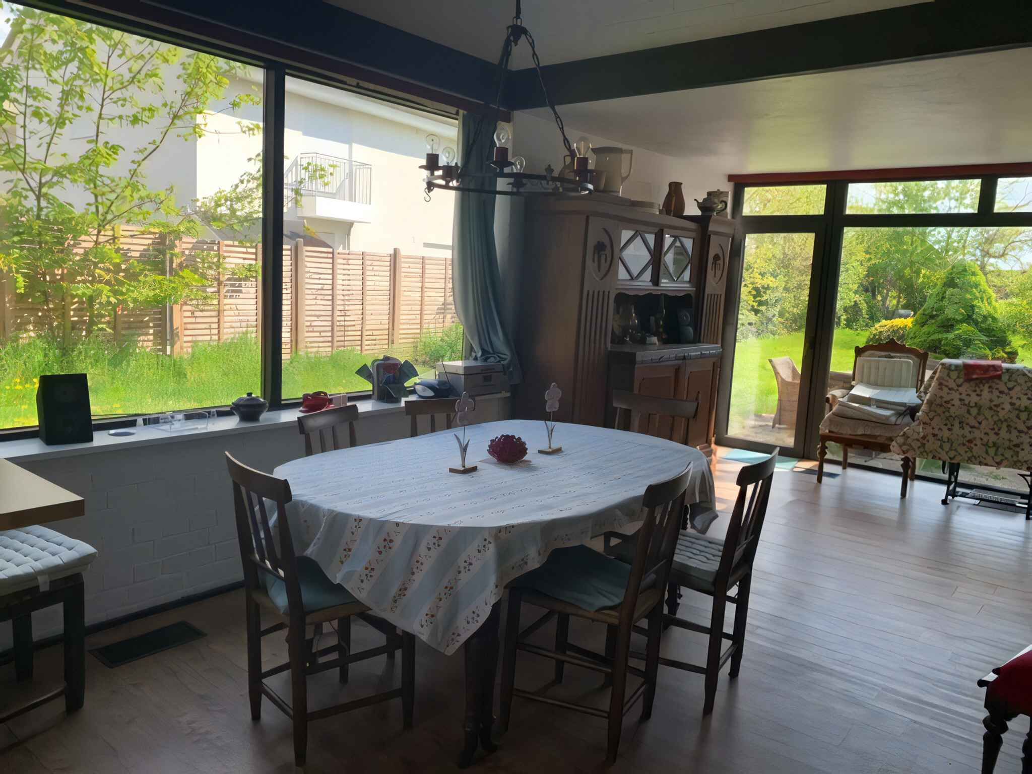 A dining area with a round table, chairs, and a view of a garden through large windows.