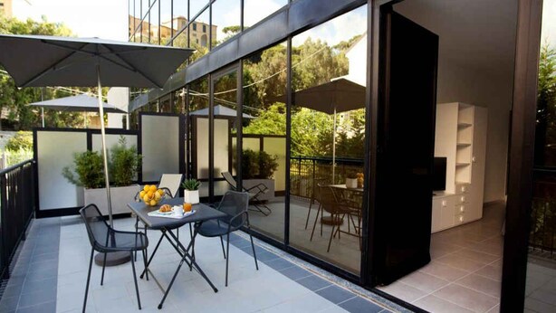 A modern outdoor patio with a table and chairs, a glass door leading to an interior space, and a view of the surrounding area.