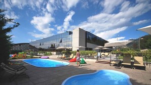 A modern building with a glass facade, outdoor pools, and lounge chairs.