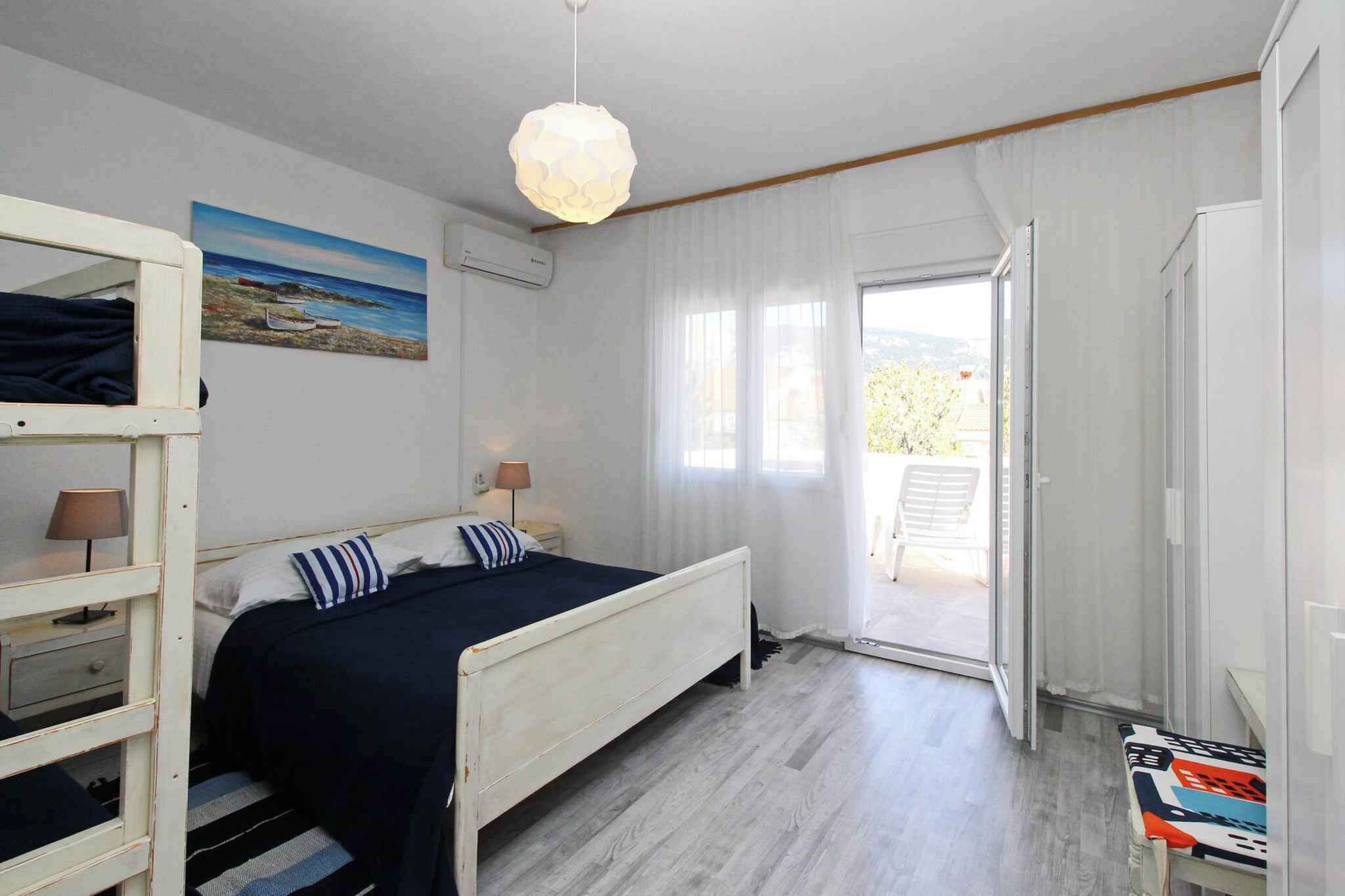 Ein Schlafzimmer mit einem Bett, einem Etagenbett, einem Gemälde, einer Klimaanlage, einer Pendelleuchte und Blick durch eine Tür in einen Außenbereich.