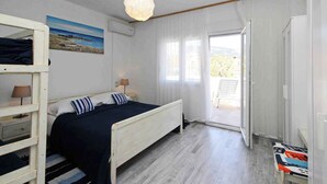 A bedroom with a bed, a bunk bed, a painting, an air conditioner, a hanging light fixture, and a view through a door to an outdoor area.
