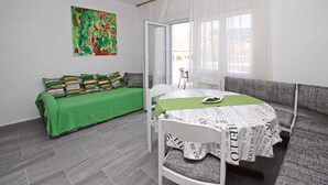 A modern room with a green sofa, a white dining table with a patterned tablecloth, and a colorful abstract painting on the wall.