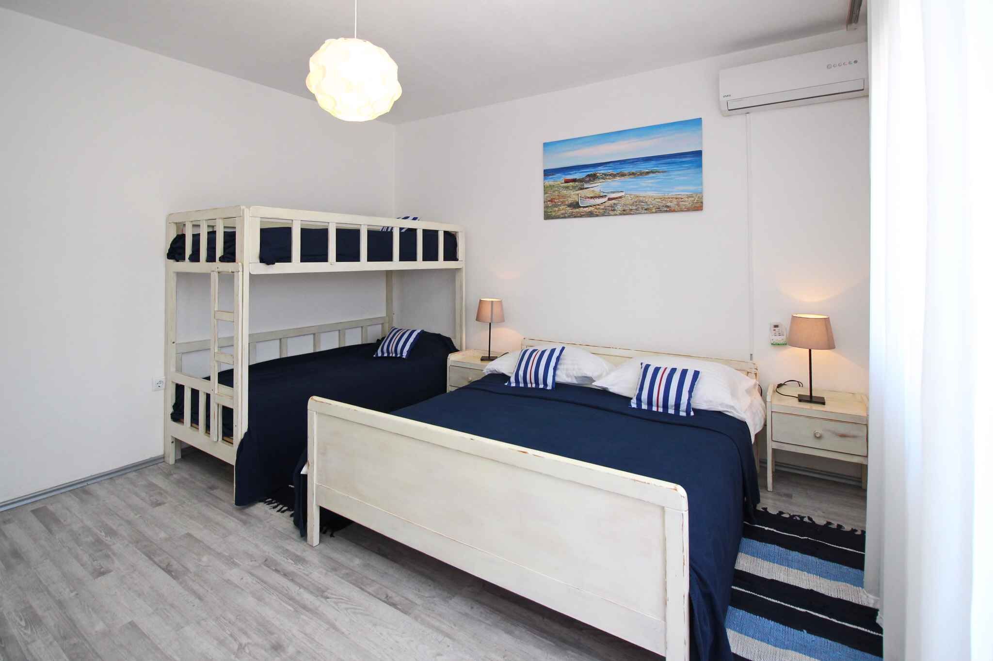 A bedroom with bunk beds, a bedside table with a lamp, a wall-mounted air conditioner, and a painting of a beach scene.