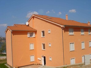 Ein zweistöckiges Gebäude mit rotem Ziegeldach, zahlreichen Fenstern mit Fensterläden und einer Satellitenschüssel.