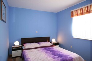 Ein Schlafzimmer mit einem Bett, zwei Nachttischen, einem Fenster mit Vorhängen und einem Wandbild.