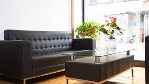 A black leather sofa and ottoman in a room with wooden flooring, a glass coffee table, and two potted plants.