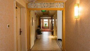 A hotel hallway with a red carpet, a potted plant, and a decorative wall light.