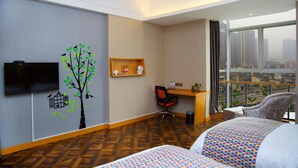 A hotel room with a large window, a desk, two beds, a TV, and a wall decoration.