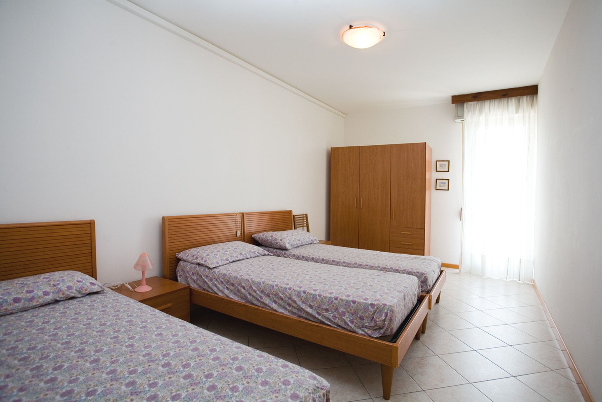 Un dormitorio con dos camas individuales, un armario de madera y una mesita de noche con lámpara.