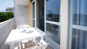 Un balcone con tavolo e sedie bianche, una porta scorrevole in vetro e vista sul mare.
