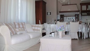 Een woonkamer met een witte bank, een eettafel gedekt met witte tafelkleden, en een keuken in de achtergrond.