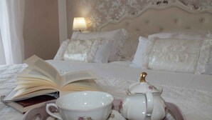 Een net opgemaakt bed met een lamp, een boek, een theepot en een kopje op een dienblad.