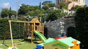 A playground with a slide and swings, a small playhouse, and a stone wall. - Holiday apartment mit Klimaanlage und Pool (Loano)