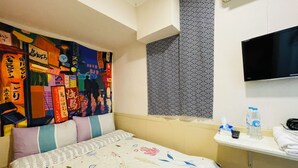 A hotel room with a bed, a wall tapestry, a patterned wall, a TV, and a small shelf with toiletries. - Cindy Hostel (Kowloon)
