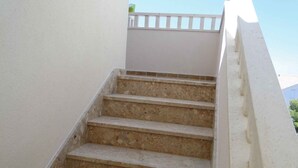 Un escalier en béton avec une rampe blanche, menant à un balcon blanc.