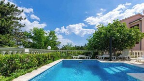 A rectangular swimming pool with clear blue water, surrounded by lush greenery and white lounge chairs.
