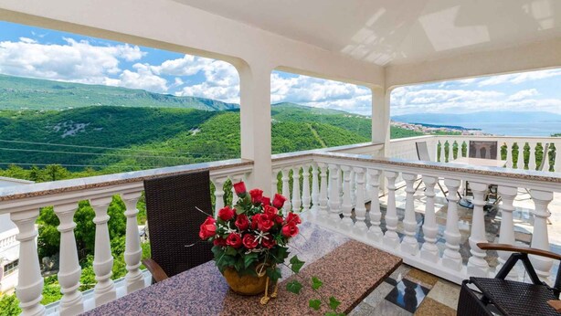 A balcony with a view of green hills and a body of water.