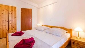 A single-bed room with a wooden headboard, white bedding, two bedside lamps, and a wooden wardrobe.