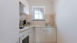 A compact kitchen with white cabinets, a built-in oven, a coffee maker, and a window above the sink.