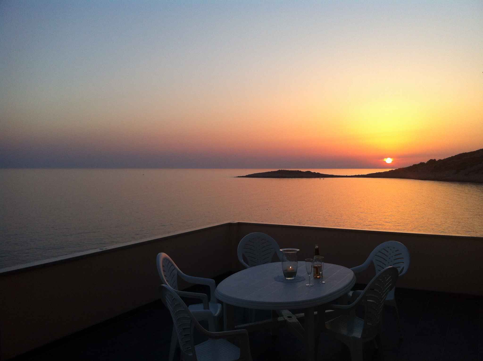 A table with chairs facing a sunset over the sea.