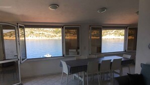 Un balcón con una mesa y sillas, con vista a una masa de agua donde se divisa un barco a lo lejos.
