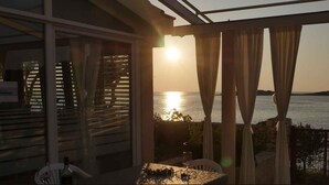 Un balcón con vistas a la puesta de sol sobre el mar, cortinas y una mesa con un vaso.