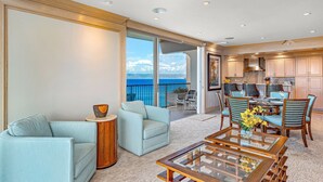 Un'ampia zona giorno con balcone vista oceano, una sala da pranzo con sedie a righe blu e una cucina con mobili in legno.