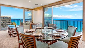 Un'area pranzo con tavolo in vetro, sedie e vista sull'oceano.