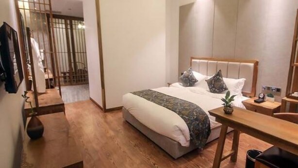 A modern bedroom with a wooden floor, a bed with a headboard, a bedside table, and a nightstand. - Jiali Inn Tidu Branch (Chengdu)