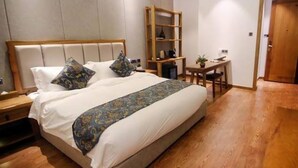 A neatly made bed with a wooden headboard, a bedside table, and a small desk with a chair. - Jiali Inn Tidu Branch (Chengdu)