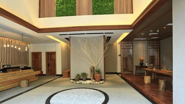 Eine geräumige Lobby mit einer zentralen Dekorationsecke, die einen Baum und Kübelpflanzen, Holzbänke und einen gemusterten Boden zeigt.
