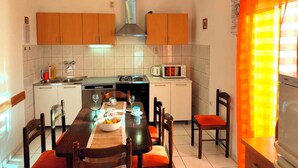 Una cocina con armarios de madera, una estufa a gas, un microondas y una mesa de comedor preparada para cuatro personas con sillas color naranja.