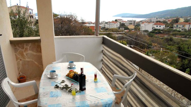 Un balcón con una mesa para dos personas, una botella de vino y una cesta de fruta.
