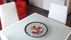 Un salon moderne avec une table blanche, des chaises rouges et blanches, un canapé rouge et un mur en briques blanches.