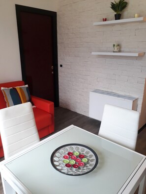 A modern living room with a white table, red and white chairs, a door, and a brick wall with shelves. - Holideal Campione Giulia Exclusive (Tremosine)