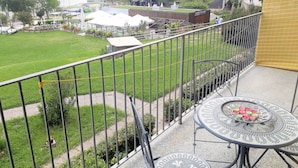 Un balcon donnant sur un espace verdoyant, avec une clôture en métal et une table sur laquelle est posé un bol décoratif.