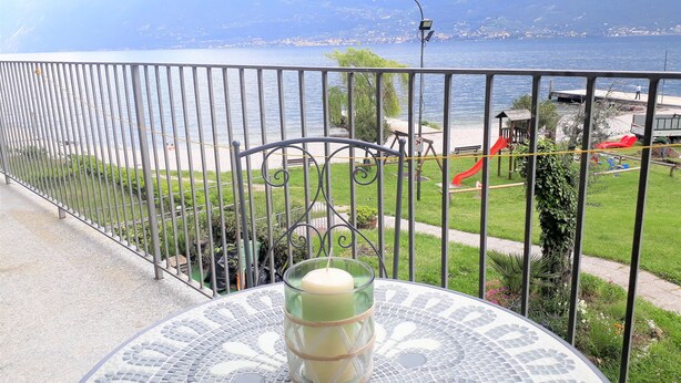 Un balcon avec vue sur un lac et des montagnes, une clôture en métal et une table avec une bougie.
