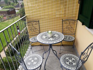 Un balcon avec une table ronde et deux chaises, une porte verte et un moustiquaire jaune.