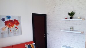 Un salon moderne avec un canapé rouge, un tableau de fleurs et des murs recouverts de briques blanches disposées en motif.