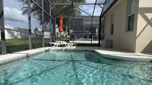 A clear swimming pool with a glass enclosure, surrounded by a white deck and a covered patio area.
