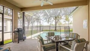 A covered patio with a glass table and chairs, a grill, and a view of a swimming pool.