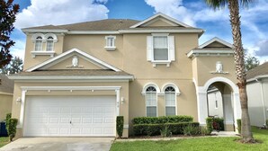 A two-story house with a garage, a driveway, and a palm tree.