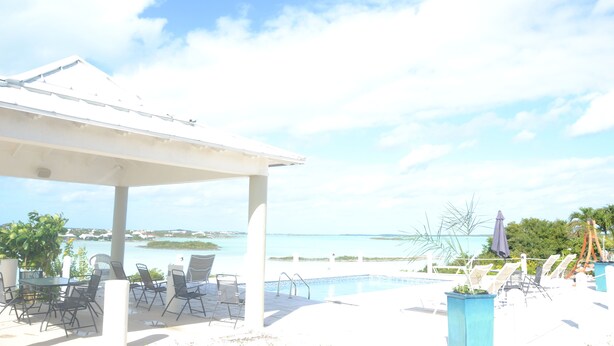 Área de piscina externa com espreguiçadeiras e um espaço de estar coberto com vista para a água.