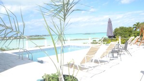 Área da piscina com espreguiçadeiras e vista para o oceano.