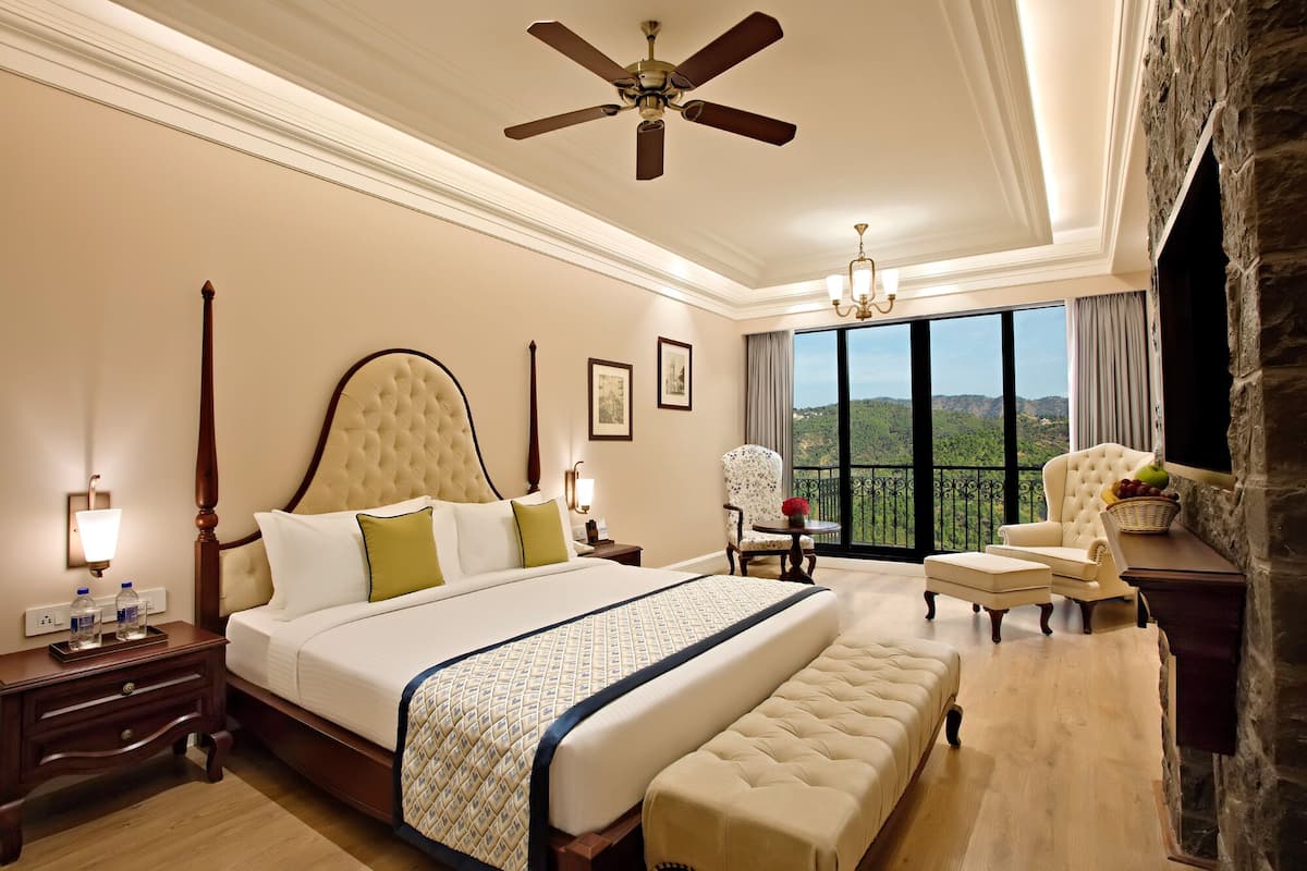 A spacious bedroom with a large bed, a sitting area with a view, and a balcony.