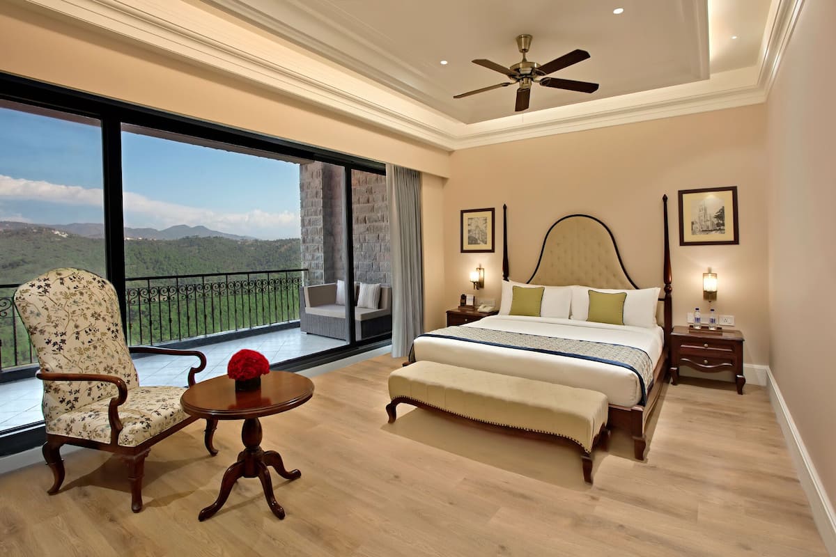 A spacious bedroom with a large bed, a sitting area, and a balcony with a scenic view.