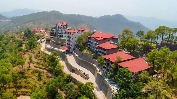 A multi-story hotel with red roofs, situated on a hillside with a view of surrounding greenery and distant mountains.