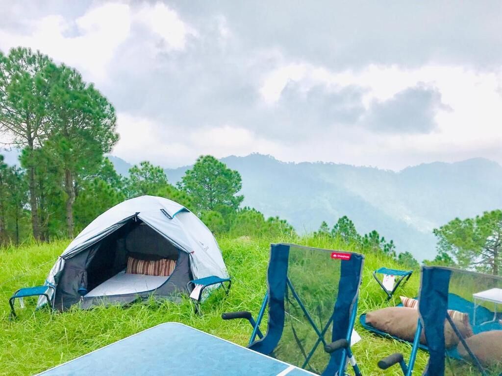 A tent set up in a grassy area with chairs and a table, surrounded by trees and hills in the background.