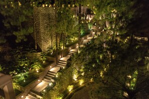 A nighttime view of a terraced garden with stone steps and illuminated pathways, surrounded by dense trees.